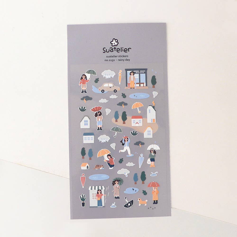 Suatelier Rainy Day town scene sticker sheet with illustrated people holding umbrellas, houses, puddles, bus stop, and clouds on grey background, made in South Korea