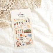 Suatelier Home Sweet Home boho decor sticker sheet with illustrated rattan chair, green sofa, string lights, plants, vases, picture frames, and sleeping cat, made in South Korea